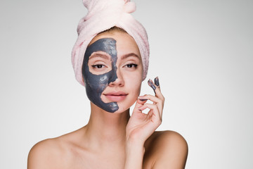 a young attractive girl with a pink towel on her head applied a useful clay mask to half the face