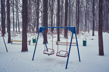 Empty swing in winter time with snow.