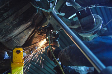 the employee of the service station produces body repair with a  Angular grinding machine in hand. sparks from the grinder disk. car service, car repair