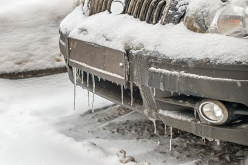 front part of the car, in winter in icicles and mud the frozen bumper, the radiator grille and the hood covered with snow