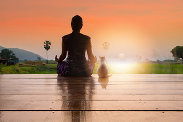 Silhouette Thai woman doing meditation and yoga with her cat over sunrise in the morning..