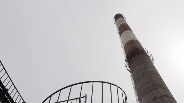 Industrial factory red and white pipe under gray cloudy sky on cold day slow motion upward panoramic shot