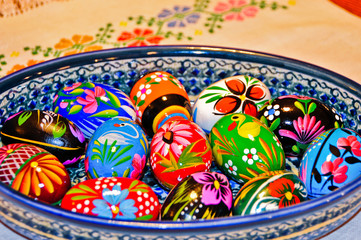 Colorful Hand Painted Wooden Easter Eggs in a Ceramic Bowl on a cloth with a needlepoint flower design.