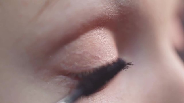 Green eyed unrecognisable caucasian girl puts black make up mascara on eyelash with brush, detail close up, slow motion