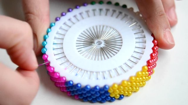 A seamstress woman pulls out and removes a pin with plastic head from a set of white discs. Dressmaker get a multi-colored needle and put it back