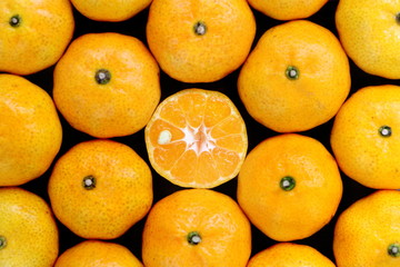 Top view of many orange on black background have middle piece was sliced see the seed inside.