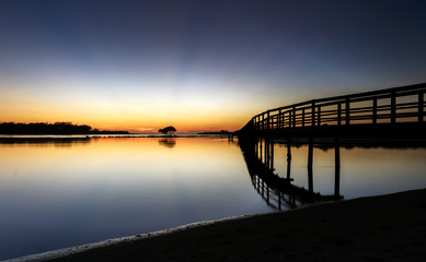 Fototapeta na wymiar Sunrise with a lone tree and a jetty