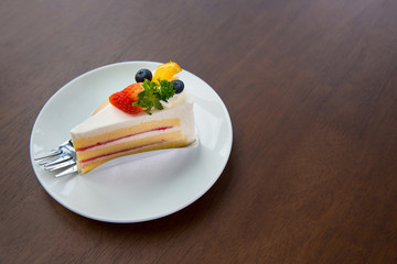 Fruit cake with whip cream topping strawberry and blueberry and orange on wooden table