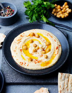 Hummus, chickpea dip, with spices in a black plate on grey stone background.