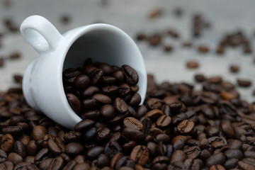 Coffee beans spilled out of white ceramic cup