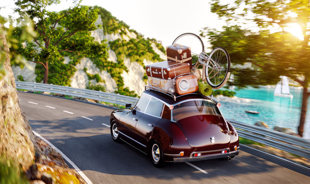 Cute little retro car with suitcases and bicycle on top goes by the road along beautiful harbor between mountain in summer day.