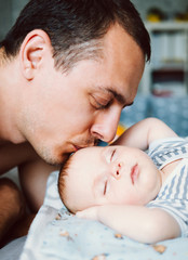 Happy young father looking with tenderness at his sleeping baby girl and kissing her.