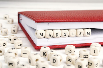 Word Marxism written in wooden blocks in red notebook on white wooden table.