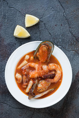 White plate with buyabes fish soup over cracked weathered asphalt background, top view, vertical shot