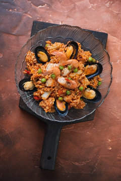Plate of spanish seafood paella on a fire warm rusty metal background, view from above, vertical shot
