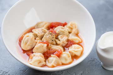 Soup with russian meat dumplings pelmeni served in a white bowl, selective focus, close-up