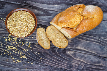 Rye bread on a wooden background near a bowl of wheat close-up.