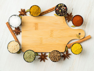 Various Indian spices in metal cups, empty wooden board, seasoning on white wooden table. top view, space for text.