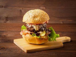 Big delicious homemade burger with beef cutlet, cheese, onion, tomato and lettuce on toasted rolls. American fast food, unhealthy eating.  Side view.