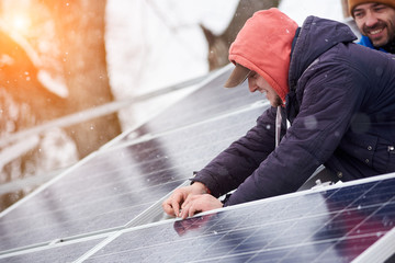 Men are engaged in the installation of solar cells in the winter. Snow is falling down
