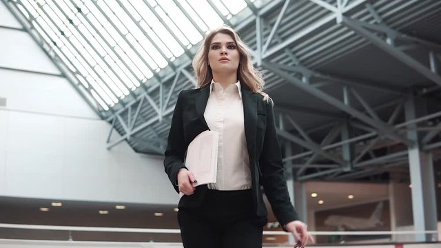 confident business woman is walking along the production building. the manager is in a hurry to meet with clients or a business partner. woman in business suit holding documents in hands