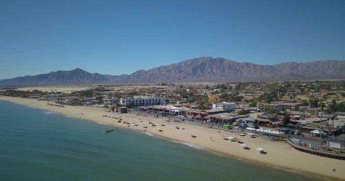 Aerial diagonal view moving backwards of the malecon San Felipe, Mexico, Baja California waterfront and beach with a boats and swimmers.