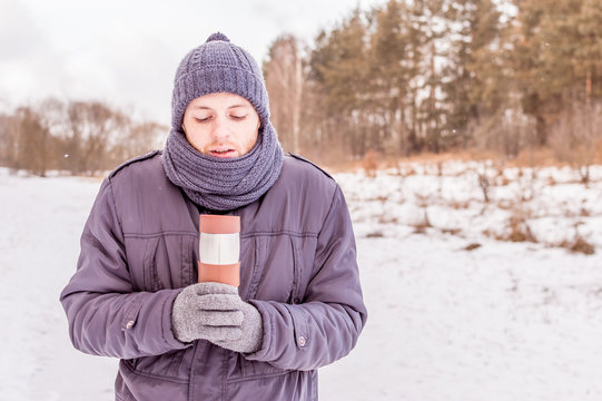 young man holds thermos in the woods in winter