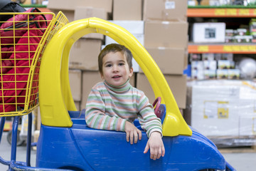 The boy 4 years in a striped jacket is sitting in a children's typewriter in a construction shop