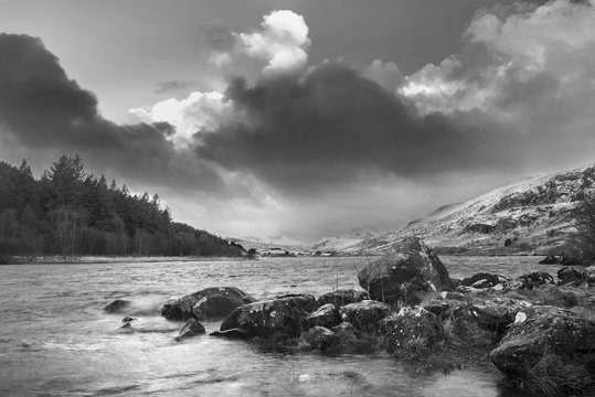Beautiful  black and white Winter landscape image of Llynnau Mymbyr in Snowdonia National Park with snow capped mountains in background