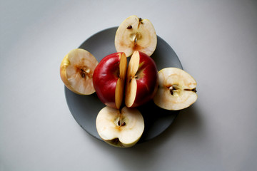 Two red and four yellow apple halves in flower shape on a grey concrete plate