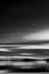 Beautiful view of Trasimeno lake (Umbria, Italy) at dusk, with black and white tones and moon in the sky