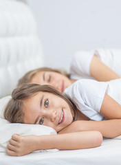 little girl lying with sleeping mother on the bed in the bedroom