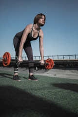Fototapeta na wymiar Woman working out on the roof. Brunette female doing deadlift with barbell.