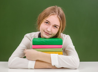 Teen girl hugs a stack of books on the background of a school board