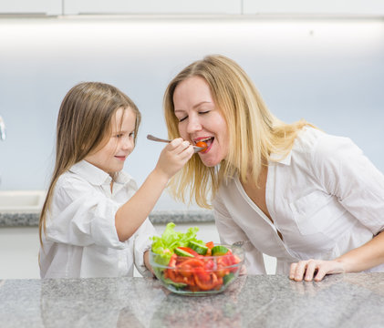 daughter feeds mom with vegetables in the kitchen