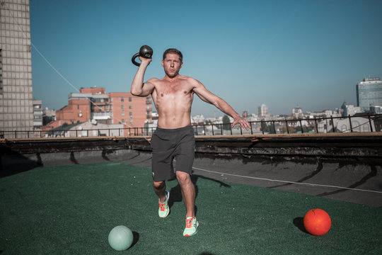 Sportive lifestyle, athletic man working put with weight. Training on the roof, sportsman lifting weight with one hand.