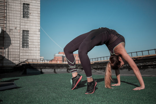 Gymnast woman training on the rooftop. Flexible sporty girl training in the sun.
