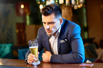 Waist-up portrait of handsome young businessman sitting at bar counter with beer glass in hand...