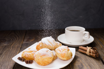 Delicious eclairs sprinkled with icing sugar, stand on a wooden table. Copy spase.