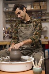Fototapeta na wymiar Artist makes clay pottery on a spin wheel in workshop