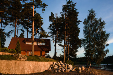 Modern russian village in national russian style on the lake coast. Good place for camping, fishing, hunting and relax. Summer sunset sky reflection in calm warm water.