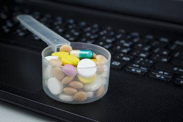 Pile of pills in a plastic measuring spoon on the keyboard