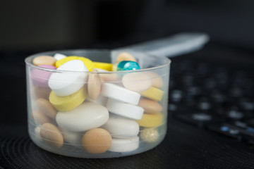 Pile of pills in a plastic measuring spoon on the keyboard