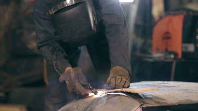 Unrecognizable worker with welding helmet on cuts off metal piece with a oxy acetylene cutting torch at a mechanical hangar