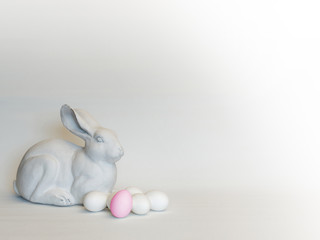 Osterdekoration: Osterhase mit Ostereiern (eines pink, die anderen weiß) in weißtoniger Farbgebung, mit Copyspace