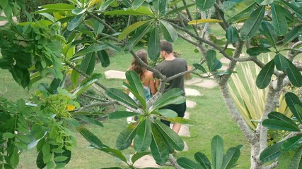 Couple holding hands of each other and walking in the tropical park. Young Man and woman going along exotic the territory of the resort. Summer vacation trip concept.