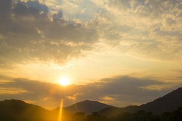 Beautiful sunset at the seaside with mountains on background. The sun breaks through the clouds. A stream of light appears from the evening sky. Sea waves. Ocean vibes.