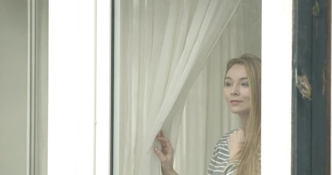 Beautiful young woman looking through window.