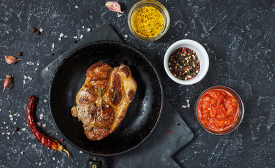 Juicy pork steak with spices on pan on dark stone background. Top