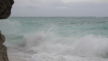 Waves crash against rocks on a beach in Bali.